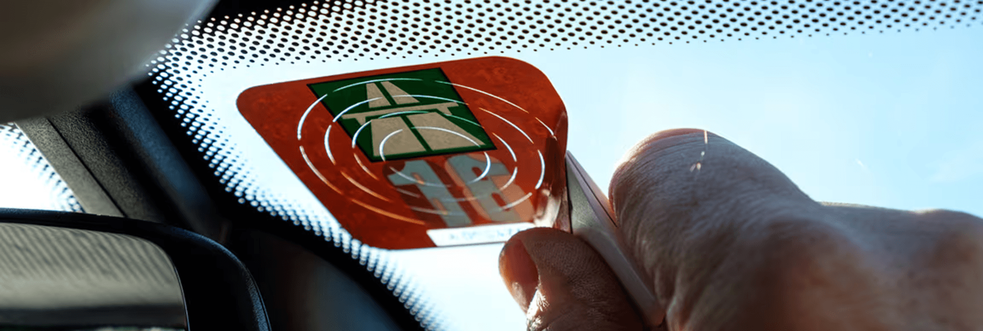 A sticker being scraped off of a windshield.